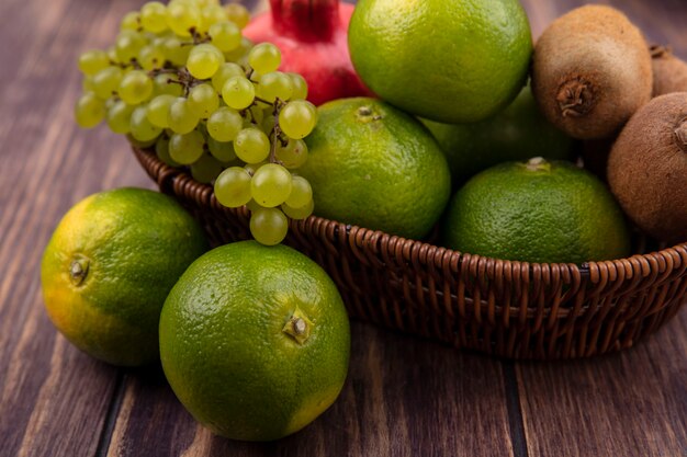 Side view tangerines with kiwi apples and pomegranate in a basket on a wooden wall