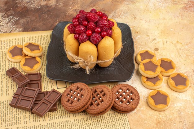 Вид сбоку вкусного торта, разного печенья на коричневой тарелке на столе смешанного цвета