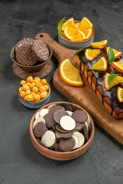 Side view of tasty cakes cut oranges with biscuits on cutting board on dark table