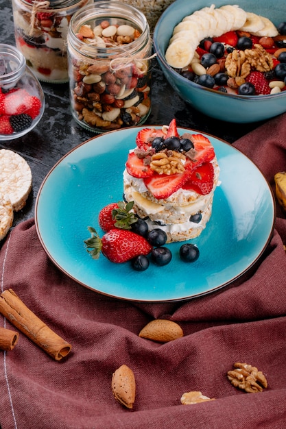 Foto gratuita vista laterale del pane croccante saporito con le fragole e i dadi maturi dei mirtilli con panna acida su un piatto ceramico sulla tavola rustica di legno