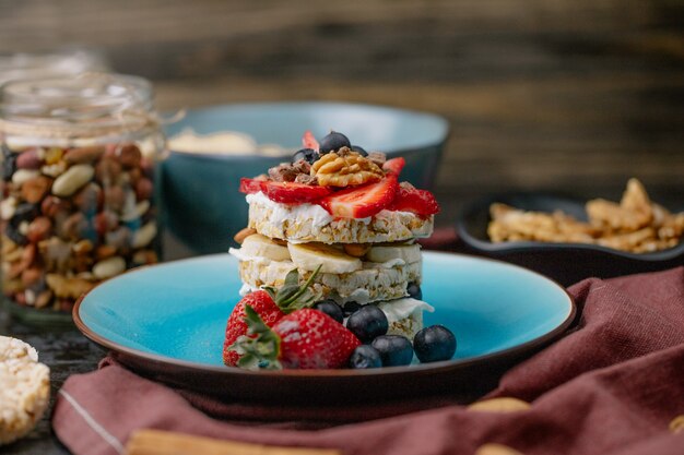 Side view of tasty crispbread with ripe blueberries strawberries and nuts with sour cream on a ceramic plate