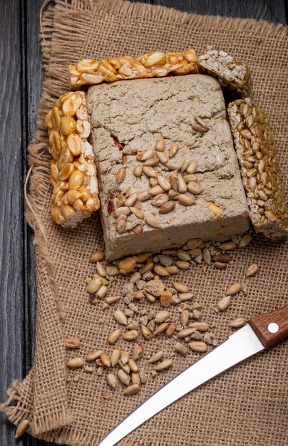 Side view of tasty halva with honey bars with peanuts and sunflower seeds on sackcloth