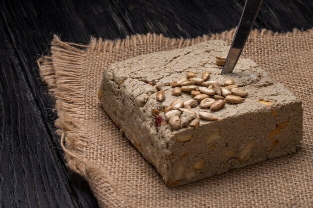 Side view of tasty halva with a knife and sunflower seeds on a sackcloth