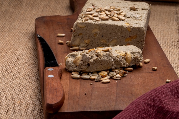 Free photo side view of tasty halva with a knife and sunflower seeds on a wooden board