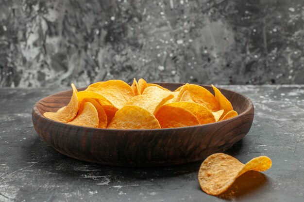 Side view of tasty homemade potato chips on a brown plate and laid on gray table