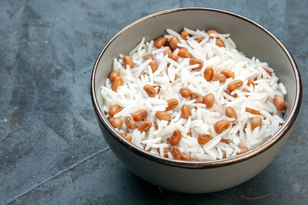 Side view of tasty rice meal with beans in a brown small pot on the left side on blue background