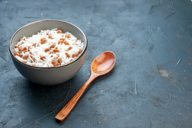 Free photo side view of tasty rice meal with beans in a white small pot and wooden spoon on the right side on blue background