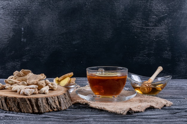 Side view a tea with ginger, slices and honey on sack cloth and dark wooden background. horizontal