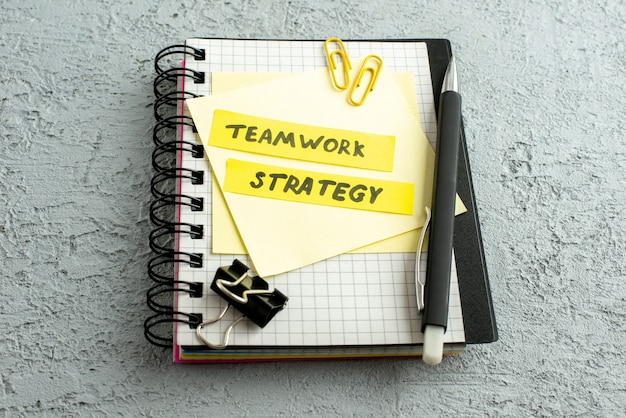 Free photo side view of teamwork strategy writings on coloured envelopes pen on spiral notebook and book on gray sand background