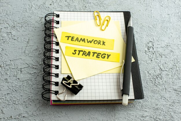 Side view of teamwork strategy writings on coloured envelopes pen on spiral notebook and book on gray sand background