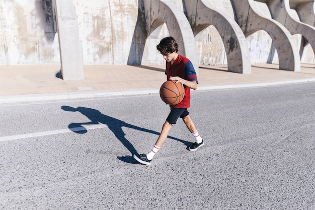 Vista laterale di un adolescente che gioca pallacanestro vicino al muro di cinta