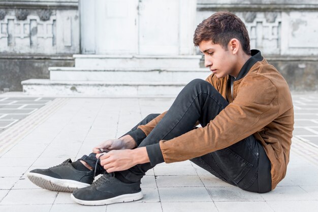 Взгляд со стороны подростка сидя снаружи и связывая его шнурок ботинок