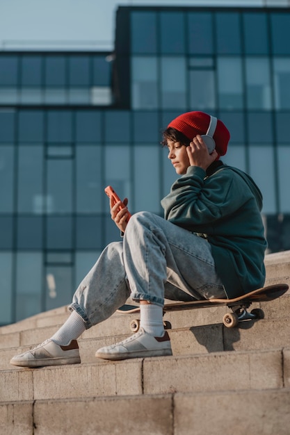 Side view of teenager outdoors listening to music on headphones while using smartphone