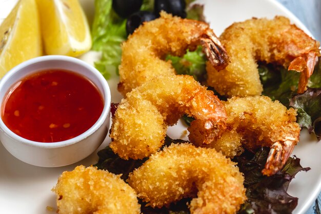 Side view tempura shrimps with sweet chili sauce slice of lemon and black olive on a plate