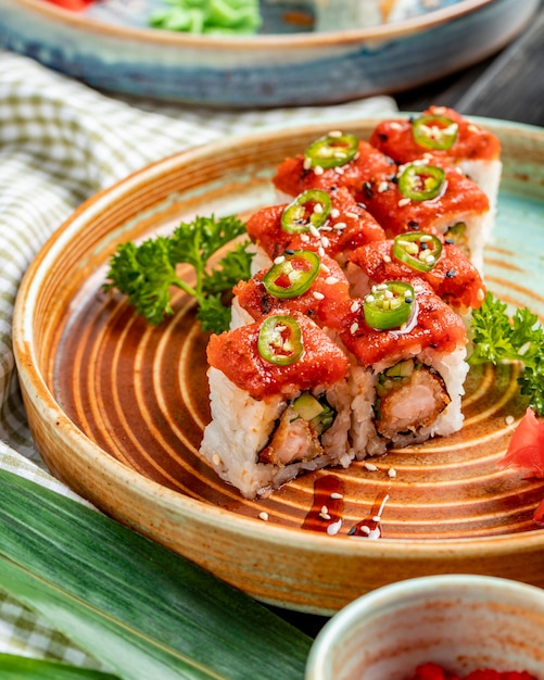 Side view of tempura sushi maki with shrimp and avocado on a plate with ginger and wasabi