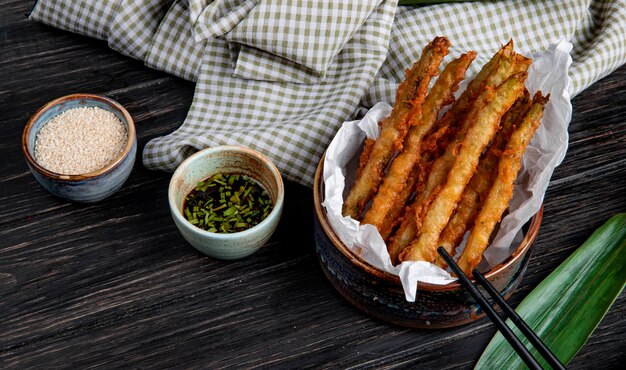 side view of tempura vegetables in a bowl served with soy sauce on wooden table with plaid fabric