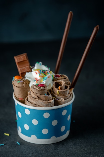 Side View of Thai Ice Cream Roll with Colorful Sprinkles in a Cardboard Bowl on Black Wall – Free Stock Photo