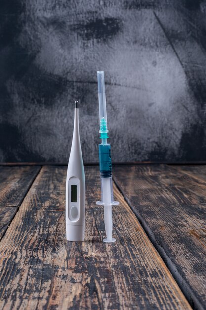 Side view thermometer and needle on dark wooden background. vertical