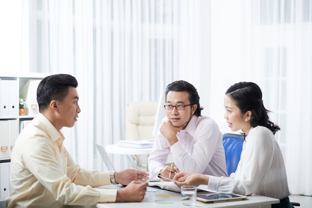 Side view of three colleagues discussing the project sitting at the office desk