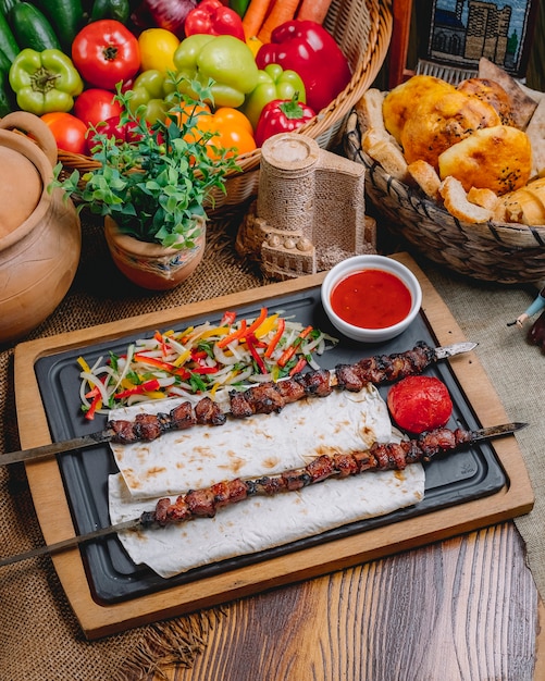 Вид сбоку тике-шашлык на шпажках на лаваш с овощным салатом и кетчупом
