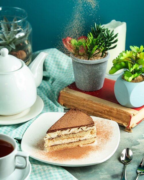 Free photo side view tiramisu dessert with a book and a plant on the table