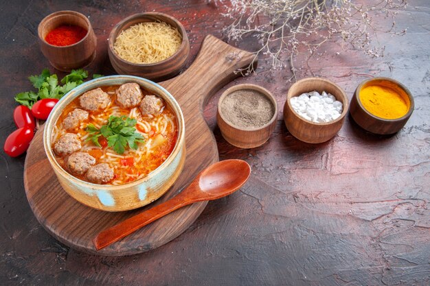 Vista laterale della zuppa di polpette di pomodoro con noodles in una ciotola marrone e diverse spezie olio bottiglia cipolla aglio su sfondo scuro image