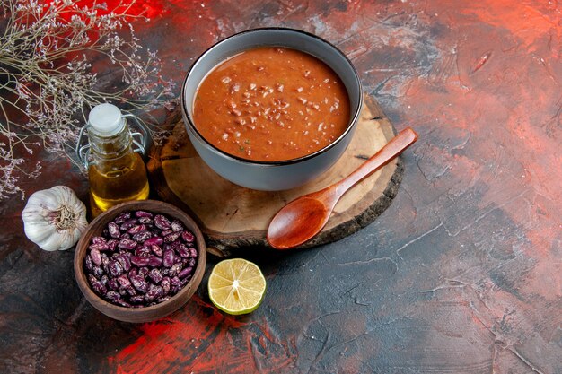 Side view of tomato soup in a blue bowl on a wooden tray beans oil bottle on mixed color table