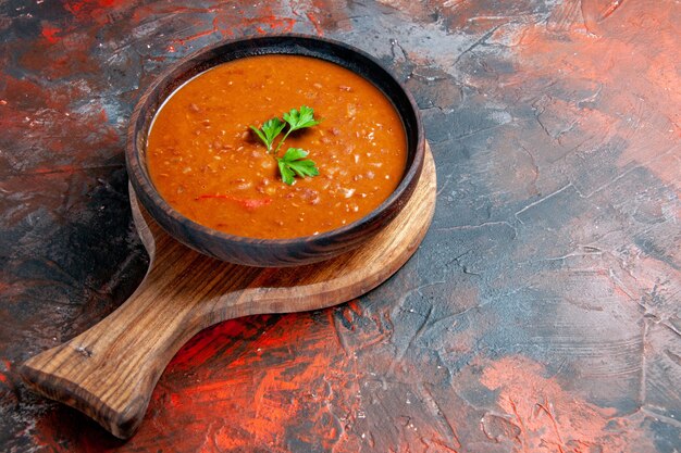 Side view of tomato soup on a brown cutting board on the right side of a mixed color table