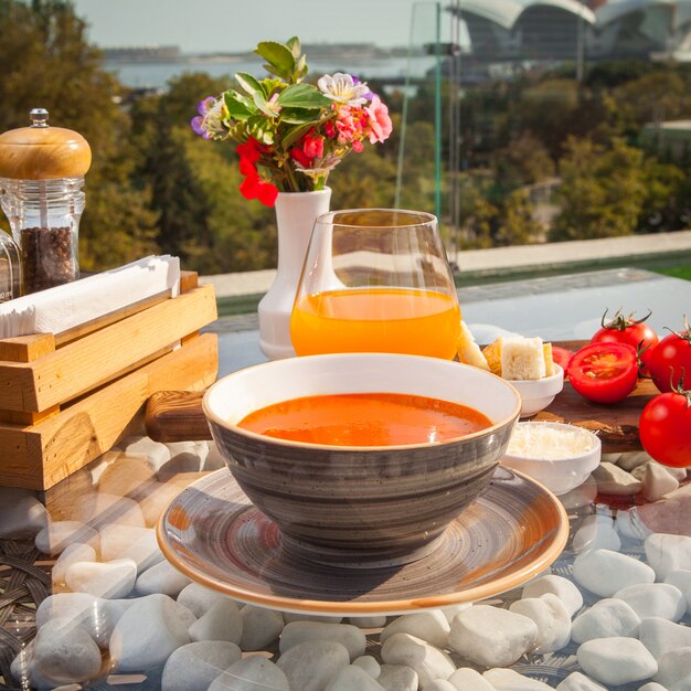 Side view tomato soup with tomato, juice on a glass table decorated with stonesat seaside restaurant