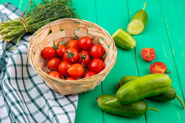 Side view of tomatoes in basket on plaid cloth and cucumber dill around on green