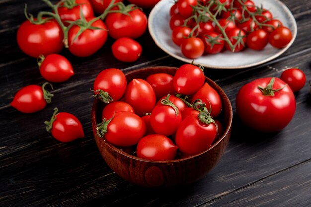 Side view of tomatoes in bowl and plate and other ones on wooden table