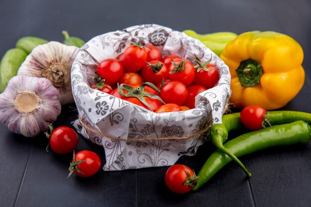 Side view of tomatoes in bowl with garlic pepper and cucumber around on black