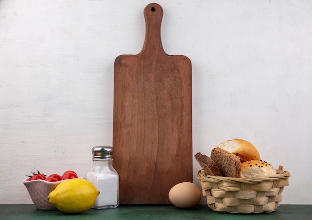 Side view of tomatoes on a bowl with lemon slat shaker a bcuket of breads on white