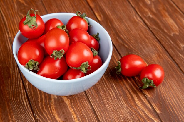 Side view of tomatoes in bowl with other ones on wooden table