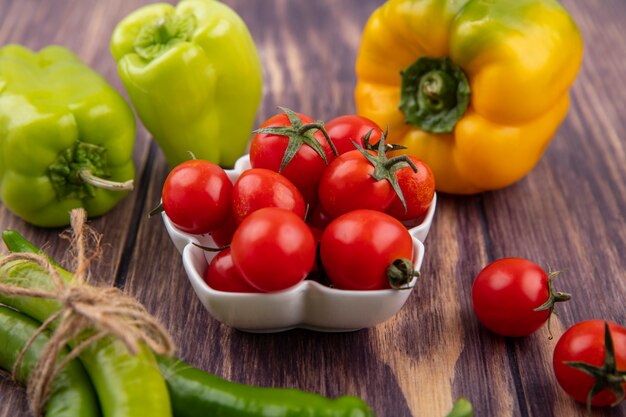 Side view of tomatoes in bowl with peppers around on wood