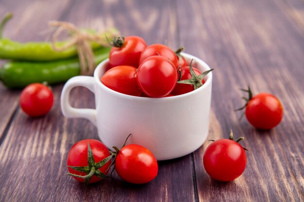 Side view of tomatoes in cup and peppers on wood