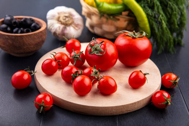 Side view of tomatoes on cutting board and olive garlic dill pepper around on black