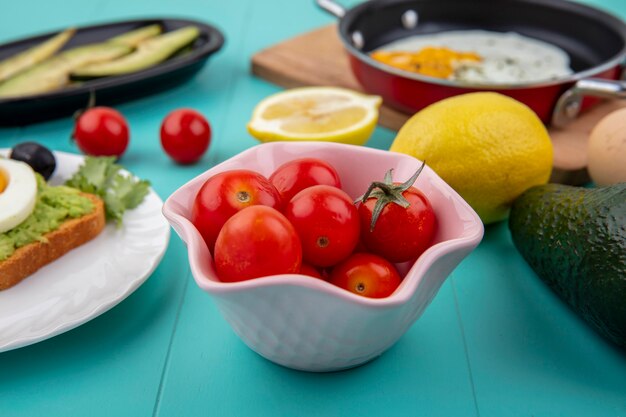 Вид сбоку помидоров на миске pinl с лимонами, яичницей на сковороде на деревянной кухонной доске на синем