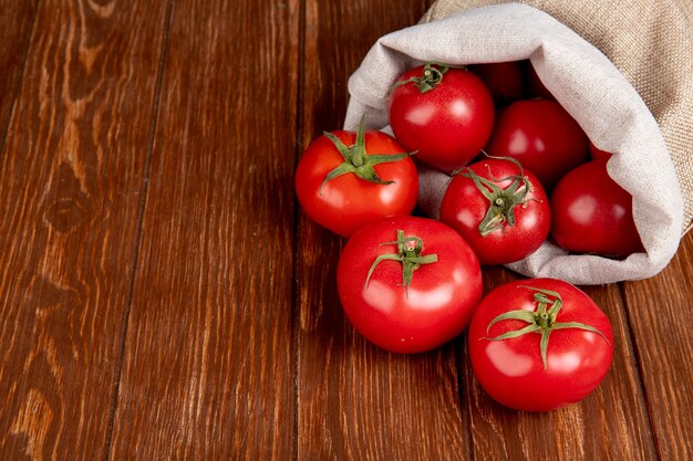 Side view of tomatoes spilling out of sack on right side and wooden table with copy space