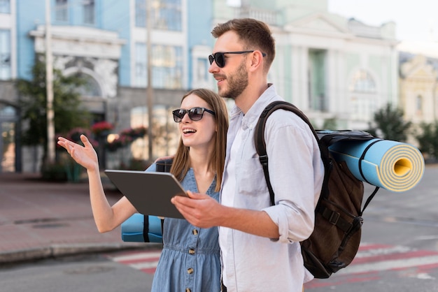 Free photo side view of tourist couple looking at tablet outdoors