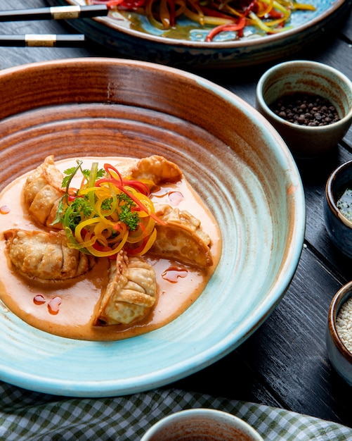 Вид сбоку традиционные азиатские пельмени с мясом и овощами, подается с соусом на тарелку на деревенском