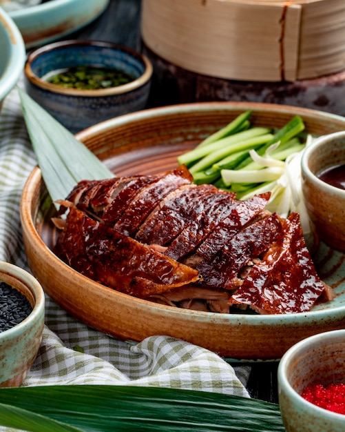 Side view of traditional asian food peking duck with cucumbers and sauce on a plate