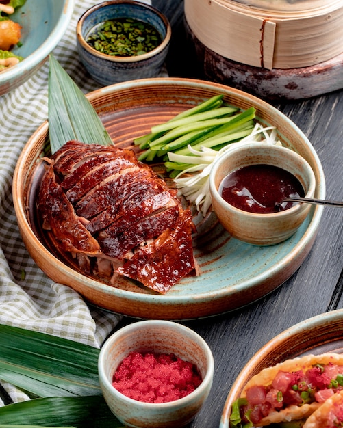 Side view of traditional asian food peking duck with cucumbers and sauce on a plate