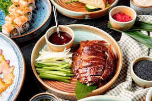 Side view of traditional asian food peking duck with cucumbers and sauce on a plate