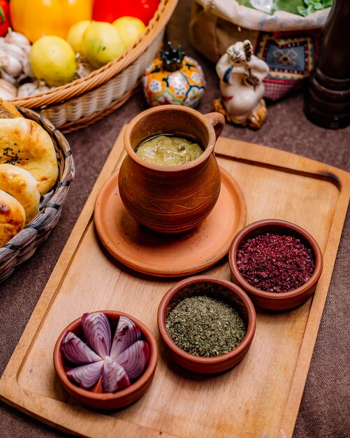 Side view a traditional azerbaijani dish piti in a pot with sumac dried herbs and onions on a tray