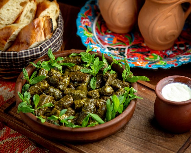 Side view of traditional dolma in grape leaves with sour yogurt on a wooden table