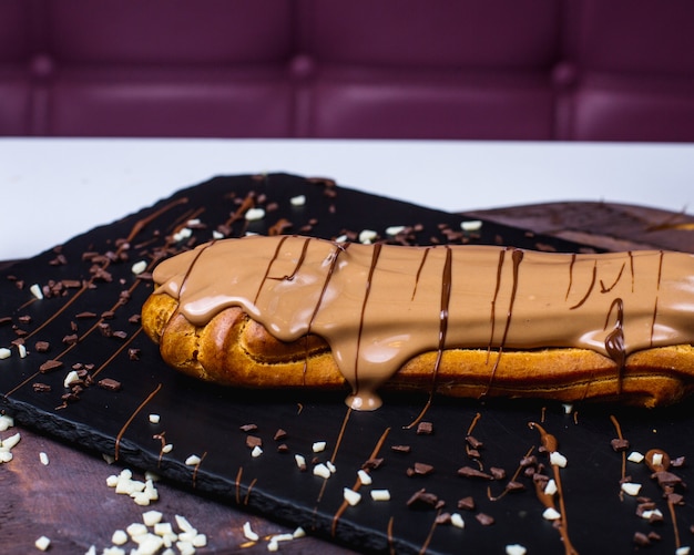 Free photo side view of traditional french eclair decorated with milk chocolate on a wooden surface