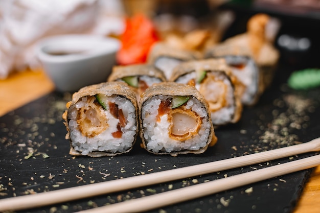 Side view of traditional japanese cuisine hot sushi roll tempura with king prawn cucumbers and cream cheese on a black board