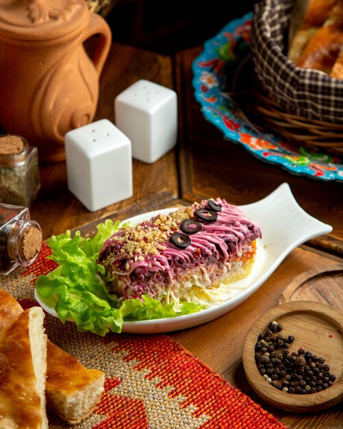 Вид сбоку на традиционную русскую кухню заправил салат из сельди слоями вареных овощей в белой тарелке на столе