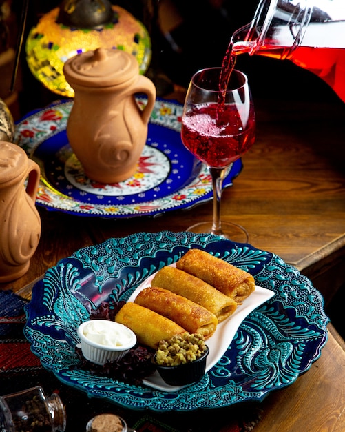 Free photo side view of traditional russian pancake rolls with meat and sour cream and lemonade pouring in a glass on a wooden table